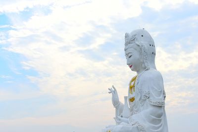 Low angle view of white buddha statue against cloudy sky