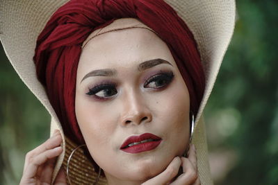 Woman looking away while wearing hat against trees