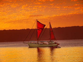 Sailboat sailing on sea against orange sky