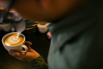 Midsection of person pouring milk in coffee cup at cafe