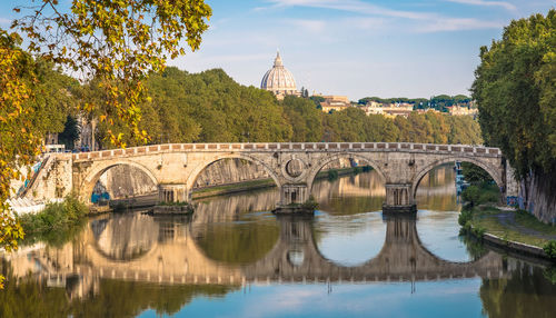 Arch bridge over river by buildings against sky