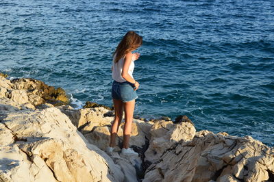 Full length rear view of woman standing on rocks at sea shore