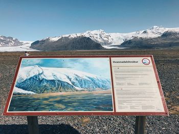 Information sign on snowcapped mountains against sky