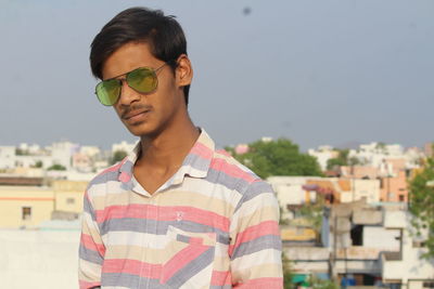 Portrait of young man standing in city against sky