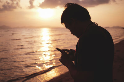 Silhouette person standing on beach against sky during sunset