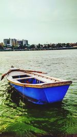 Boat moored on river by buildings in city against sky