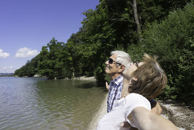 Senior couple standing at lakeshore against trees