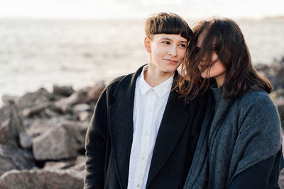 Lesbian women embracing while standing on rock against sea and sky