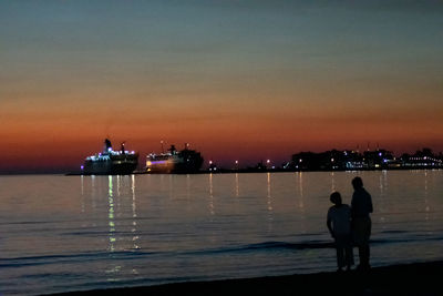 Silhouette people standing by sea against sky during sunset