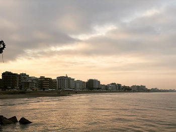 Sea by buildings against sky during sunset