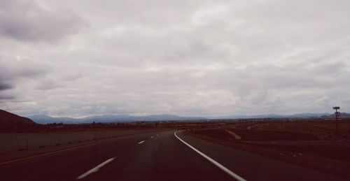 Road passing through landscape against cloudy sky