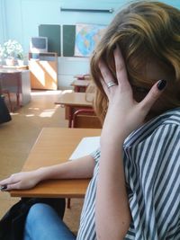 Woman with hands covering face sitting at desk in classroom