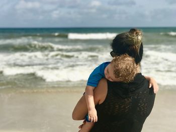 Rear view of siblings standing on beach against sky