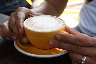 Cropped image of person holding coffee at table