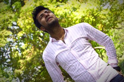 Young man looking away against trees