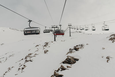 Ski lift over snow covered mountains against sky