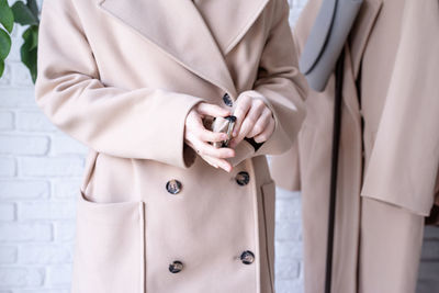 Woman in beige coat standing in front of hanger rack and choosing outfit dressing. selection of 