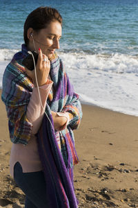 Young woman holding sunglasses while standing on beach