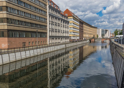 Canal by buildings in city against sky