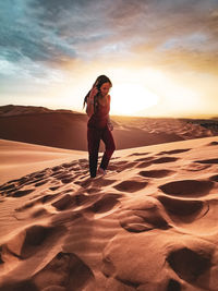 Full length of woman walking on sand dune during sunset