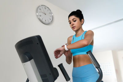 Young woman training at the gym using eliptical crosstrainer looking at her smart watch