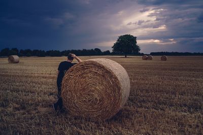 Man with hay bales on field against sky