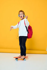 Portrait of young woman standing against yellow background