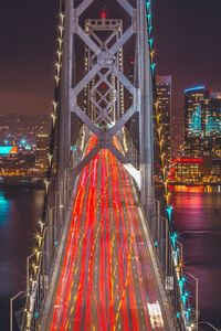 Light trails on illuminated city against sky at night