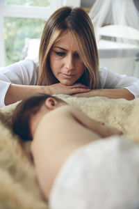 Mother looking at sleeping daughter on bed at home
