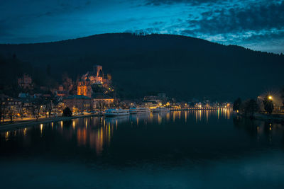 Illuminated buildings by lake against sky at night
