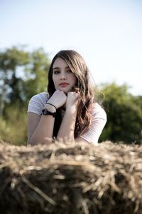 Portrait of teenage girl leaning on hay bale against clear sky