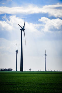 Wind turbines on landscape against clouds