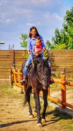 Happy woman riding horse with boy at ranch on sunny day