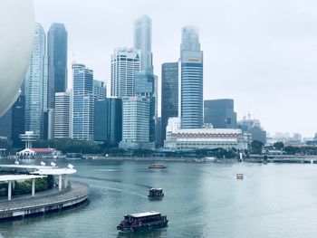 Boats in river by buildings in city against sky