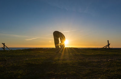 Unrecognizable man silhouette doing yoga on green lonely seaside with a beautiful sunset sky on background