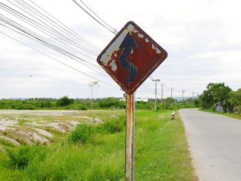 Road sign on field against sky