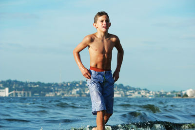 Shirtless boy walking in sea against sky