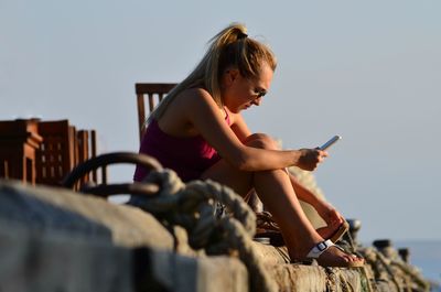 Young woman using mobile phone against sky