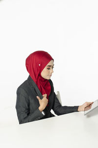 Young woman looking away while sitting against white background