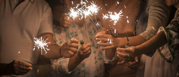 Midsection of friends holding lit sparklers