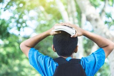 Rear view of boy holding books on head in park