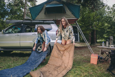 Smiling friends with sleeping bags at campsite in forest