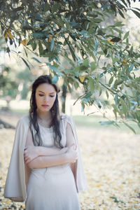 Thoughtful fairy elf young woman with arms crossed standing at park