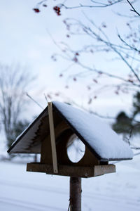 Snow covered birdhouse on field against sky