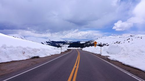 Empty road leading towards snowcapped mountains against cloudy sky