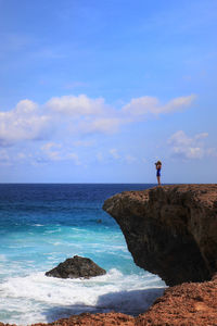 Woman standing on rock by sea against sky