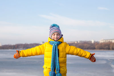 Girl with arms outstretched standing on frozen lake against sky