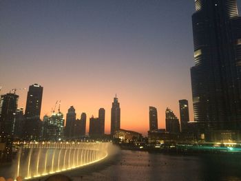 Illuminated buildings in city against clear sky at dusk