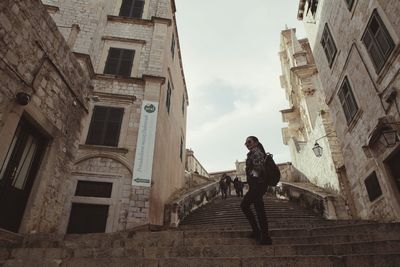 Low angle view of woman walking on staircase amidst buildings