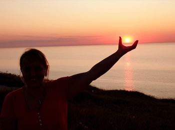 Optical illusion of woman holding sun at beach against sky during sunset
